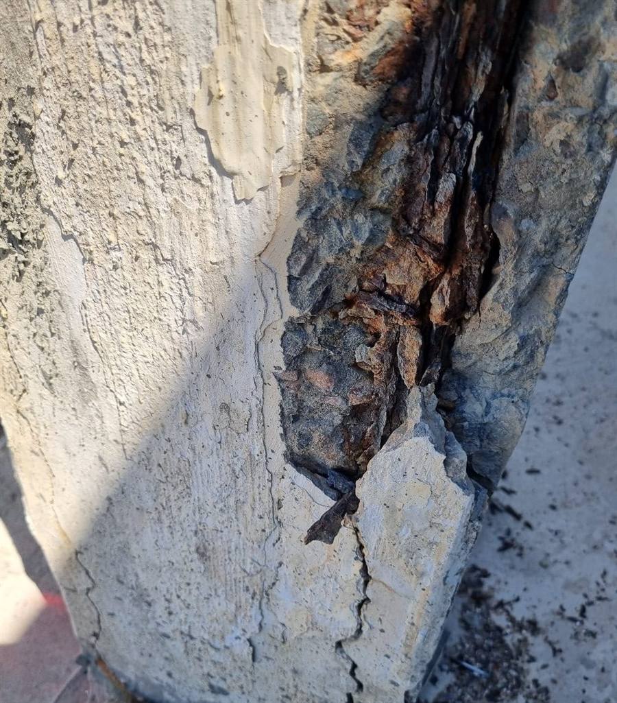 Detalhe de vistoria técnica: corrosão de armadura exposta em pilar de concreto, evidenciando patologia estrutural